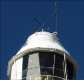 Photograph showing view of white lantern roof dome with dark coloured weathervane on top of dome. Glazing panes of lantern room are positioned below the dome in a circular formation