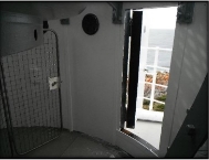 Photograph showing doorway access onto balcony from inside lantern room. Door out onto balcony is open, and a mesh metal security gate can be seen inside lantern room 