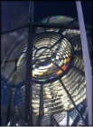 Photograph showing large lighthouse lens. Lens can be seen through glass glazing panes of the lantern house 