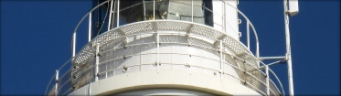 Photograph showing white balcony surrounding lantern house. White handrails ring the balcony. 