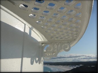 Photograph showing white, lattice catwalk. Catwalk is bolted into external lantern house walls with ornate-style bracket.