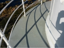 Photograph showing grey balcony floor. An arched stone surface with white balustrades and railing embedded on the edge of the balcony.