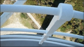 Photograph showing close up of white stanchion embedded in grey balcony floor. Access track on ground below can be seen in background. 