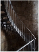 Photograph showing grey lattice stairs. The steps are embedded in the wall and wraps around and down to a lower level. Wrought iron handrails are attached to the inside of the stairs from the base of each step. 