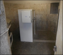 Photograph showing a small granite room with an upright, white cabinet fixed to the middle of the room. 