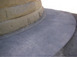 Photograph shows base of a granite stone tower, with a concrete ring around the perimeter of the base. 