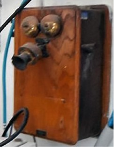 Photograph showing a timber box mounted on a wall. Telephonic equipment is attached to the front of the box. 