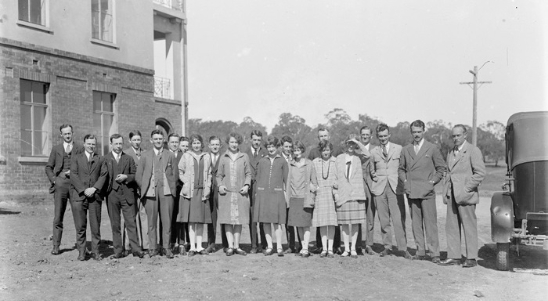 A group of approximately 20 men and women standing outside a brick building.