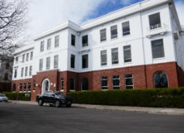 Three storey building with a brick base and rendered upper floors.  A projecting form contains a circular ground floor entrance with three windows above.