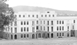 Black and white photograph of two wings of a building linked at ground floor by a recessed screen wall with three arches.