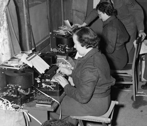 Two people in uniform typing at a machine.

