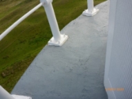 Photograph showing thin, curved, grey concrete balcony floor. White stanchions are bolted to edge of balcony floor. 