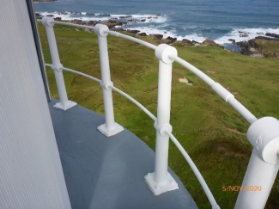 Photograph showing thin, curved, grey concrete balcony floor. White stanchions are bolted to edge of balcony floor. 