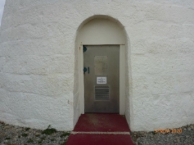 Photograph showing arched doorway entry. Stainless steel door is closed and a vent is fixed to base of tower door. 