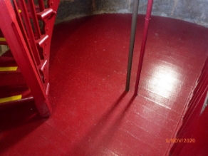 Photograph showing red timber floor. Red steps can be seen to left ascending to a floor above.