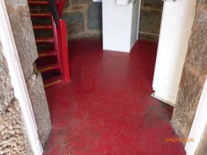 Photograph showing red floor through stone doorway. The foot of red spiral stairs can be seen extending from the floor. 