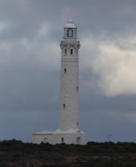 A photograph containing a white lighthouse tower against a grey sky. 