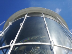 Photograph showing curved glazing panes fitted within white frames. Large lens can be seen through glazing behind.