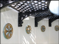 Photograph showing a section of black lattice catwalk fitted along curved, white wall. Four round vents embedded in wall panels below catwalk.
