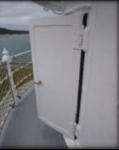 Photographs showing white lantern room door standing ajar. Door opens onto narrow balcony with curved, white balustrades pictured behind.