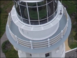 Photograph showing lighthouse lantern house with grey balcony wrapped around house with white balustrades.