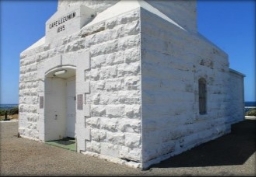 Photograph showing base of white, stone lighthouse tower with a doorway and window embedded within walls.