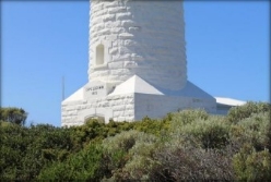 Photograph showing base of white stone lighthouse tower behind thick, green scrub.