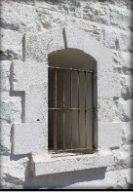 Photograph showing window opening with external grilles cut into white stone walls. 