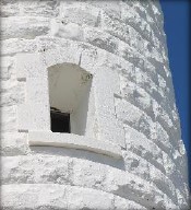 Photograph showing section of white, curved stone wall with window cut into stone.