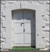 Photograph showing a white door cut into stone walls.