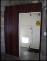 Photograph showing timber doorway fitted to internal entrance of room. Pair of door leaves seen behind.