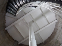 Photograph showing internal face of round, stone room. White underside of round floor above supported by while pole and floor beams. Black spiral stairs leading up to the white floor.