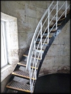 Photograph showing black, cast iron staircase with white wrought iron railing and stanchions. wrapped around stone wall.
