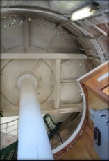 Photograph showing internal face of round, stone room. White underside of round floor above supported by while pole and floor beams. 