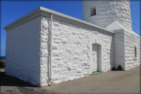Photograph showing white, stone store building attached to base of tower. 