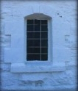 Photograph showing large window set in white, stone wall.