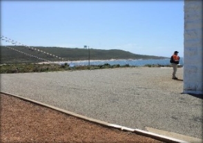 Photograph showing large asphalt paving. Ocean and man seen in background.