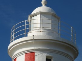 Photograph showing white lantern room of red and white lighthouse. White iron pipe rails wrap around lantern room. 