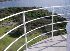 Photograph showing curved, white iron pipe railing fitted to edge of grey balcony.