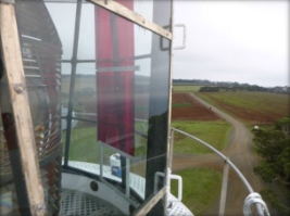 Photograph showing glazing pane fitted into astragal of lantern room. Prismatic lens can be seen behind pane, and fields are seen below in the background. 