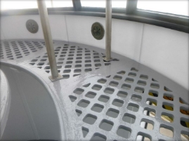 Photograph showing grey, curved lattice floor panels running along edge of lantern room. 