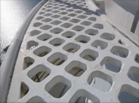 Photograph showing white, curved lattice floor panels fitted to external lantern room walls. Ocean can be seen in background. 