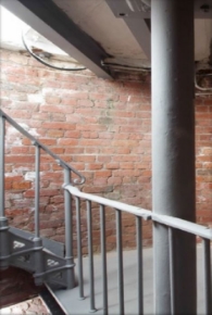 Photograph showing curved red brick wall. A set of grey stairs ascends to a level above.