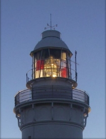 Photograph showing illuminated lantern house at dusk. Light shines from lens contained behind glazing panes. 