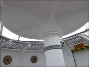 Photograph showing underside of white pedestal. Curved wall panels and lattice catwalk can be seen behind. 