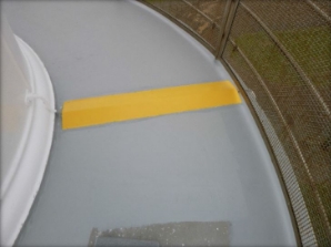 Photograph showing curved, grey balcony floor with yellow trip marker painted over conduit. Stainless steel balustrade and mesh are fitted to outer edge of balcony floor. 