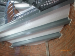 Photograph showing underside of slate floor landing, supported by iron beams and fitted into curved, red brick tower walls. 