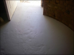 Photograph showing rounded, grey ground floor of lighthouse tower, with entry door leading outside. 