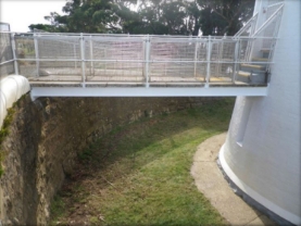 Photograph showing suspended bridge reaching from upper lighthouse entry door to top of retaining wall. 