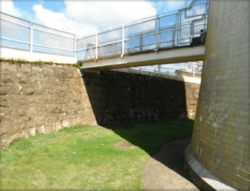 Photograph showing bridge reaching from upper lighthouse entry door to top of retaining wall. 